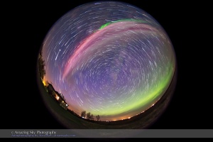 A strange red/magenta auroral arc overhead across the sky, with a more normal green diffuse glow to the north, as seen on May 10, 2015, in a stack of 80 frames taken over 45 minutes. The Big Dipper is overhead in the centre of the frame, Jupiter is at left in the west and Arcturus is at top to the south. I shot this from home, using an 8mm fish-eye lens to take in most of the sky, with the camera looking north. The 80 exposures were stacked and blended with Advanced Stacker Actions from StarCircleAcademy.com using the Long Trails effect. Each exposure was 32 seconds at f/3.6 and ISO 3200 with the Canon 6D. An individual exposure adds the more point-like stars at the start of the tapered star trails, and add the blue from the last twilight glow still illuminating the sky at the start of the sequence.