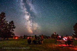 A Perseid meteor streaks down the Milky Way over the Saskatchewan Summer Star Party in the Cypress Hills of southwest Saskatchewan, at Cypress Hills Interprovincial Park, a Dark Sky Preserve. The Milky Way shines to the south. About 350 stargazers attend the SSSP every year. Observers enjoy their views of the sky at left while an astrophotographer attends to his camera control computer at right. This is a single exposure, 25 seconds, with the Laowa 15mm lens at f/2 and Sony a7III camera at ISO 3200.