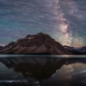 A blend of images to show the stars of the southern sky moving from east to west (left to right) over the Rocky Mountains at Bow Lake, in Banff, Alberta. The main peak at centre is Bow Peak. Crowfoot Glacier is at far left; Bow Glacier is at right below the Milky Way. A single static image shows the Milky Way and stars at the end of the motion sequence. The star trails and Milky Way reflect in the calm waters of Bow Lake this night on July 16, 2018, though they appear large and out of focus. This is a stack of 300 images for the star trails, stacked with the Ultrastreak function of Advanced Stacker Plus actions, plus a single exposure taken a minute or so after the last star trail image. The star trail stack is dropped back a lot in brightness, plus they are blurred slightly, so as to not overwhelm the fixed sky image. The sky images are blended with a stack of 8 images for the ground, mean combined to smooth noise in the ground. All are 30 seconds at f/2 with the 15mm Laowa lens and Sony a7III at ISO 3200. All were taken as part of a time-lapse sequence. Bands of airglow add the green streaks to the sky.